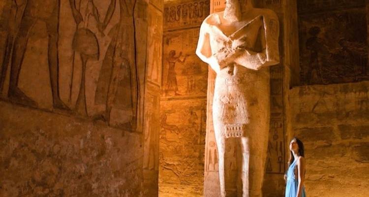 Frau steht neben großer ägyptischer Statue im Tempel.