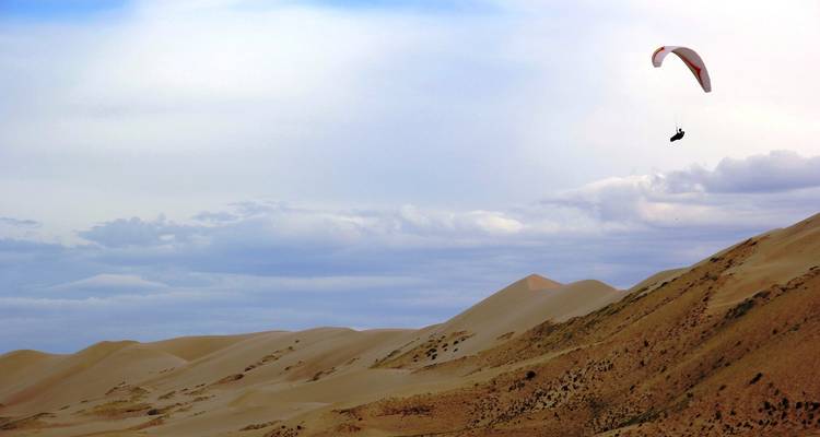 Paraglider die over woestijnduinen vliegt tegen een dramatische lucht.