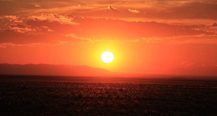 Levendige zonsondergang boven een verre bergketen gezien vanaf vlak land.