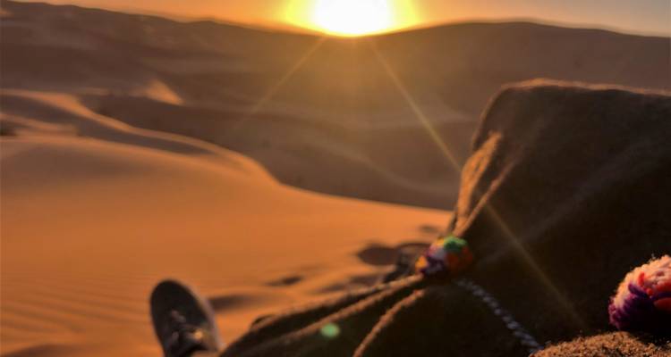 Verschwommenes Bild einer Person, die bei Sonnenuntergang auf einer Sanddüne sitzt.