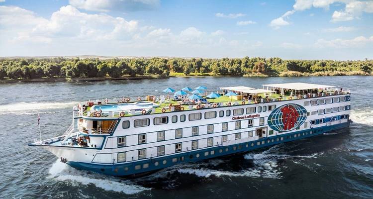 Luxury Nile cruise ship sailing on the river with a sundeck pool and passengers relaxing.