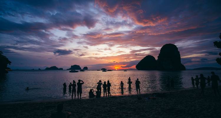 Siluetas de bañistas en aguas poco profundas observando una puesta de sol espectacular detrás de islas de piedra caliza