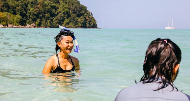 Joven mujer con snorkel sonriendo en agua turquesa cerca de una exuberante isla tropical