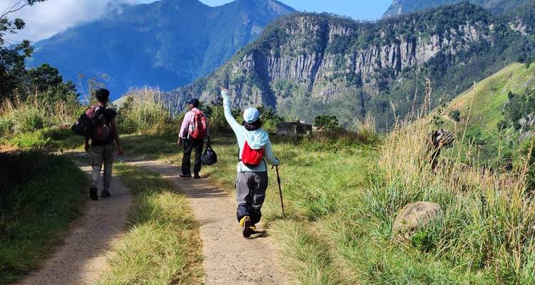 Group of hikers walking on a dirt path in a mountainous area.