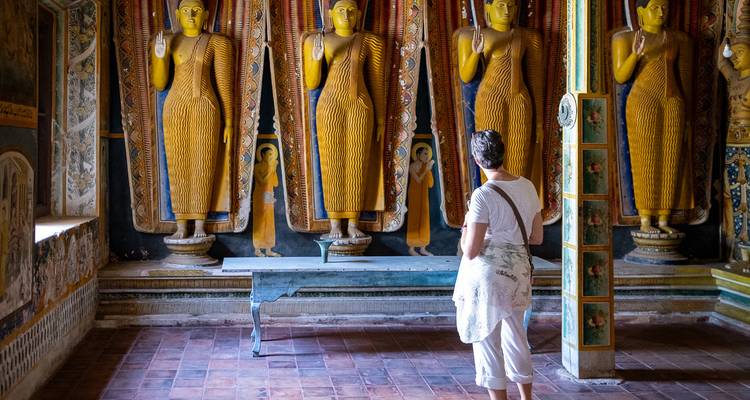 Ein Besucher betrachtet Reihen von goldenen stehenden Buddhafiguren in einer prunkvollen Tempelhal e.