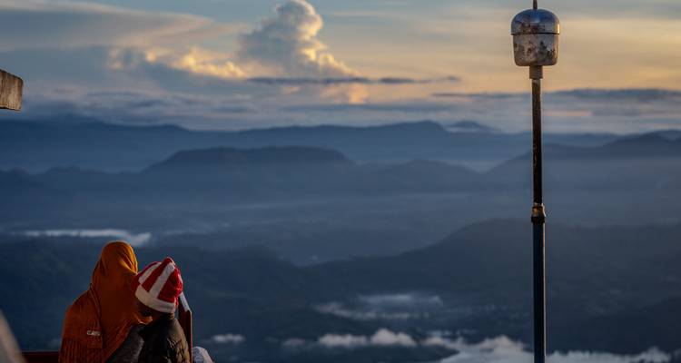 Pilger in Decken gehüllt beobachten den Sonnenaufgang über nebligen Tälern vom Adam's Peak.