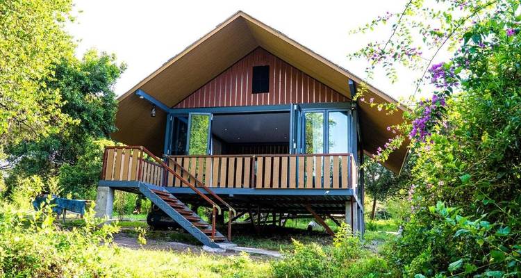 Cabaña estilo chalet rodeada de vegetación con un gran porche.