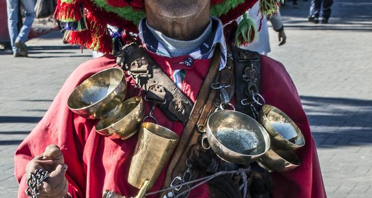 Man in kleurrijke kledij met koperen bekers en bellen.