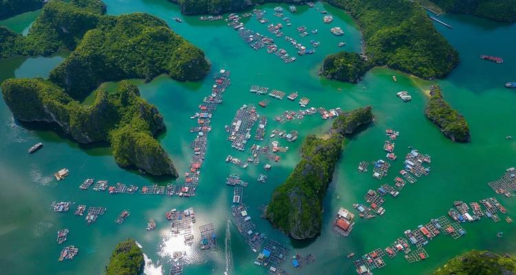Vue aérienne d'un village flottant au milieu de pics calcaires sur une eau turquoise.