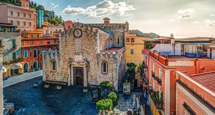 Iglesia histórica en el centro de Taormina rodeada de edificios coloridos.