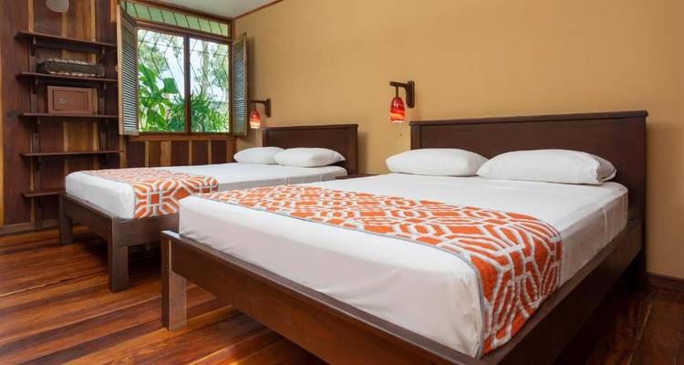 Une chambre d'hôtel pittoresque avec lits jumeaux et décoration en bois, donnant sur une végétation luxuriante.