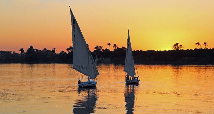 Voiliers sur une rivière au coucher du soleil.