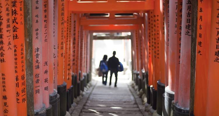 Chemin de torii avec des personnes qui marchent à travers, entouré de colonnes avec des inscriptions.
