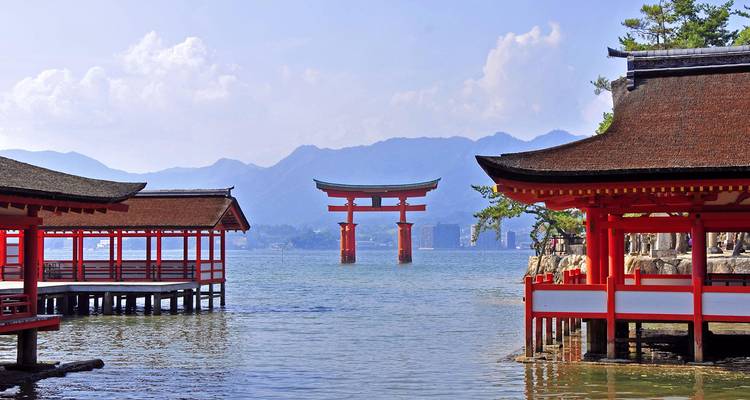 Famous red torii gate in the sea surrounded by traditional Japanese buildings.