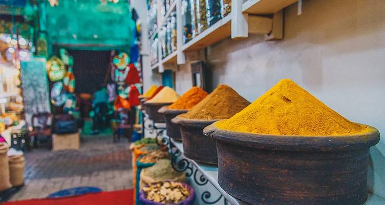 Un primer plano de especias apiladas en un mercado tradicional con colores vibrantes y gente en el fondo.