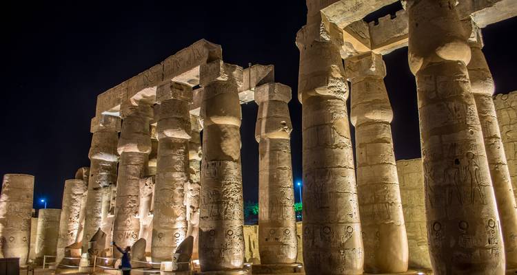 Luxor Tempel verlicht in de nacht met hoge zuilen en mensen eromheen.