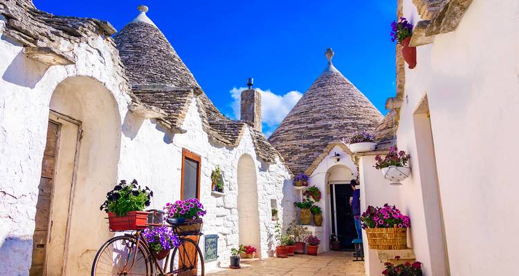 Picturesque trulli houses under a blue sky, with potted flowers.