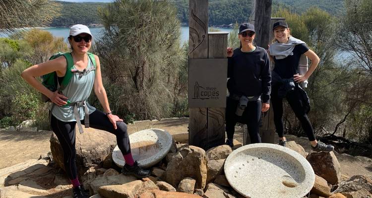 Three hikers standing by a signpost near a lake.