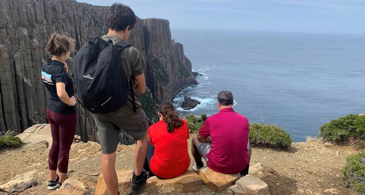 Group of people sitting on rocks overlooking a cliff and the ocean.