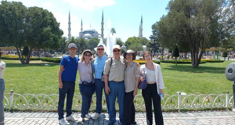 Group of people smiling and posing in front of a historic mosque with a fountain.