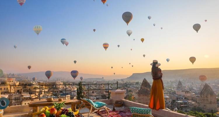 Woman overlooking a panorama of hot air balloons at sunrise.