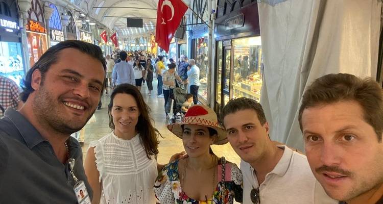 Group of friends inside a bustling marketplace with flags and shop stalls.