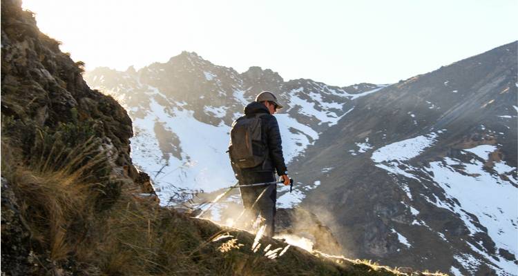 Wandelaar die loopt op een bergpad met besneeuwde pieken.
