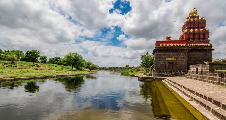 Flussufer-Tempel mit rotem Turm, der sich im Wasser spiegelt.