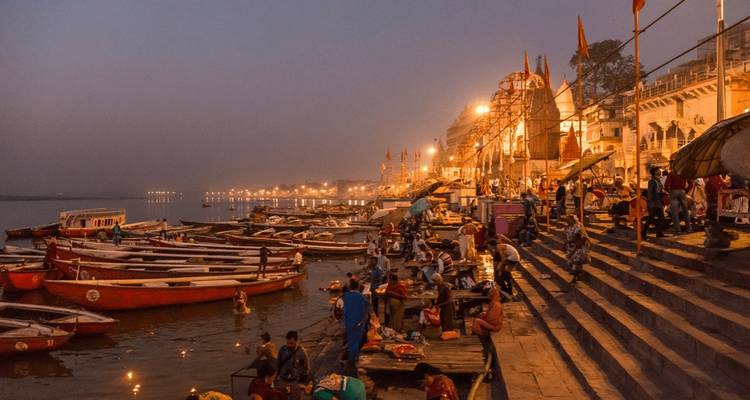 Belebte Ghats mit Menschen und Booten in Varanasi bei Abenddämmerung.