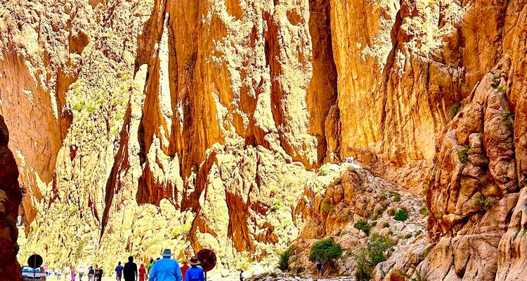 Excursionistas empequeñecidos por los imponentes acantilados color ocre del Cañón del Todra con un arroyo debajo