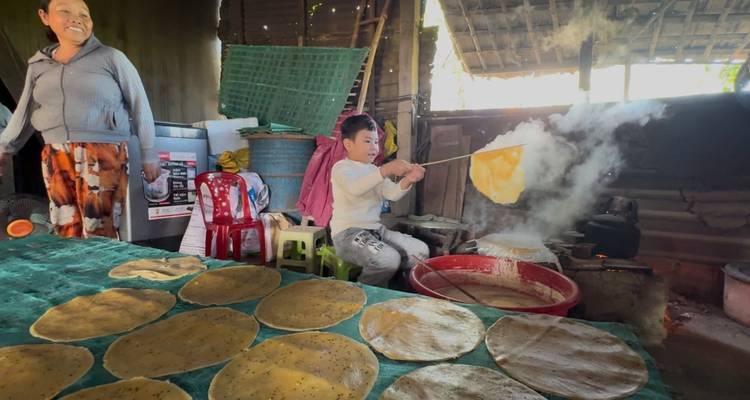 Una mujer sonríe mientras una niña voltea una galleta de arroz humeante en un fogón bajo.