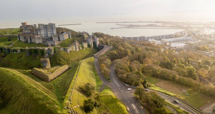 Vista aérea de un gran castillo en una colina que domina un pueblo portuario.
