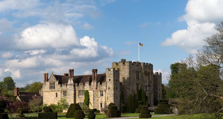 Castillo histórico con bandera en la cima y jardines bien cuidados.