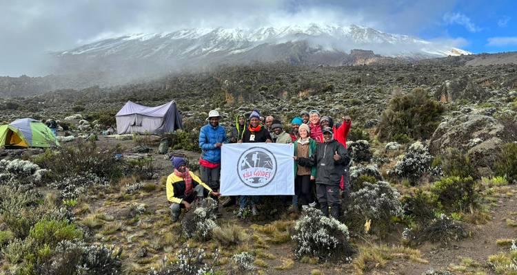 Groupe de randonneurs tenant un drapeau sur un terrain rocheux sous un ciel nuageux.