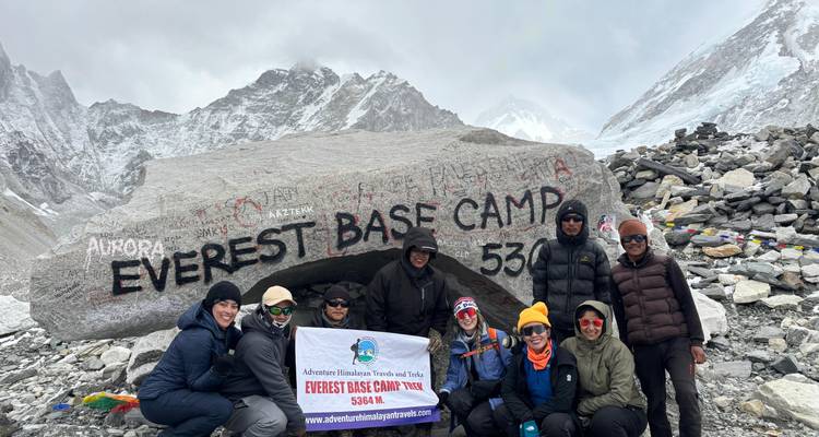 Trekkers stand beside the Everest Base Camp engraved boulder with glacier views around.
