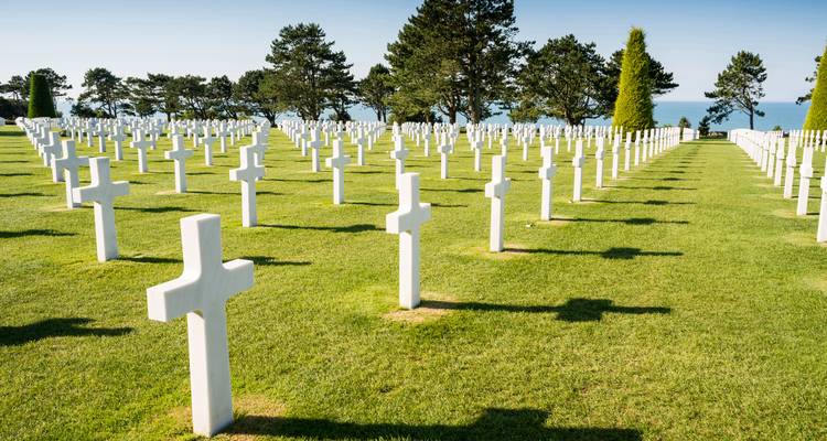 Rijen witte marmeren kruisen in een verzorgde militaire begraafplaats met uitzicht op zee.