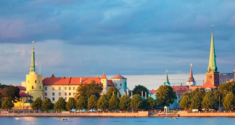 Historic buildings and a church in Riga, Latvia along a riverbank.