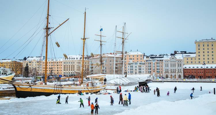 Mensen die schaatsen op een bevroren haven met schepen en stadsgebouwen op de achtergrond.