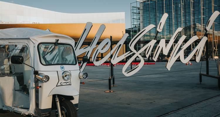 Een decoratief Helsinki-bord met een tuk-tuk bij een moderne architecturale locatie.