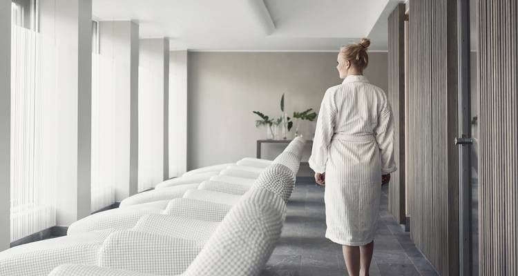 Een persoon in een badjas die loopt in een moderne spa-achtige omgeving.