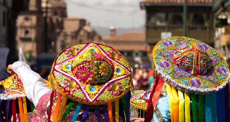 Farbenfroh bestickte andine Hüte mit Regenbogenbändern, die in einer festlichen Straßenparade in Cusco getragen werden