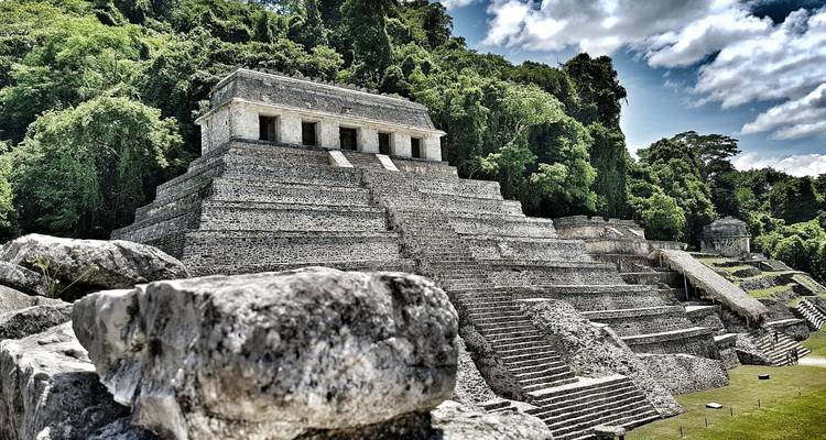 Templo de piedra del sitio arqueológico de Palenque enmarcado por una densa selva y nubes dramáticas.