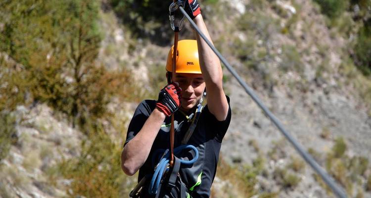Person mit Helm beim Ziplining in einer bergigen Gegend.