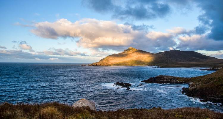 A rugged coastal headland bathed in golden light with waves crashing against rocky shores.