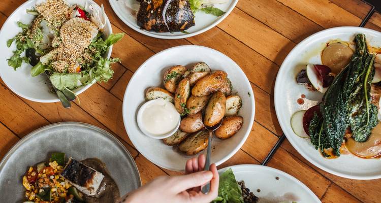 Verscheidenheid aan gerechten op een houten tafel, hand reikt naar eten.