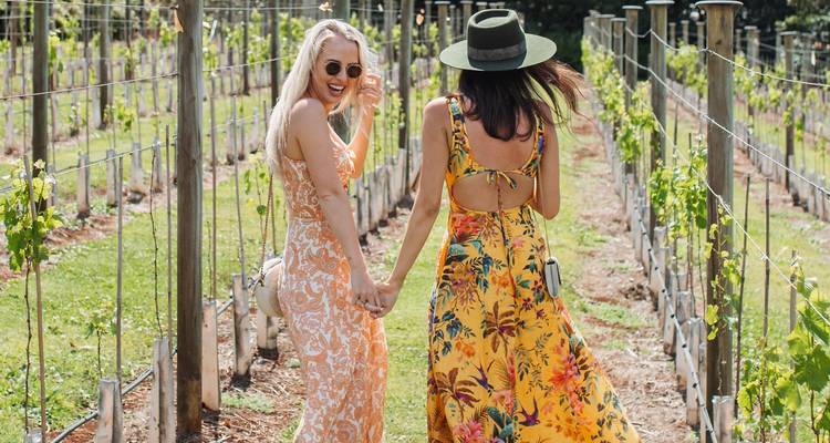 Twee vrouwen lopen door een wijngaard, gekleed in kleurrijke jurken.