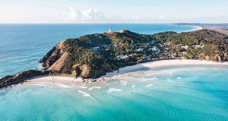 Vista aérea de una playa con un faro en una colina.