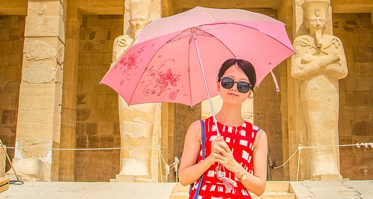 Mujer sosteniendo una sombrilla rosa de pie frente a estatuas antiguas.