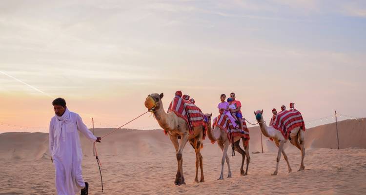 Menschen, die bei Sonnenuntergang auf Kamelen durch eine Wüste reiten