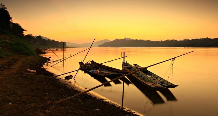 Boats resting along a riverbank during a golden sunset.